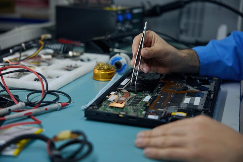 Técnico reparando placa madre de laptop con herramientas de precisión en taller de Huamachuco